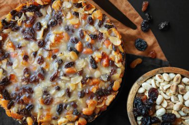 Koyu arkaplanda keten peçetelerin üzerinde tahta fındık kasesinin yanında fındıklı kuru üzümlü turta.