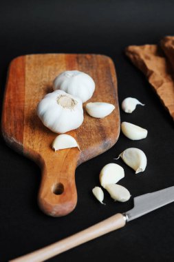 Tam sarımsak ve karanfiller tahta bir tahtanın üzerinde, arka planda bir bıçak ve keten peçetenin yanında.