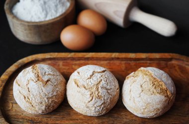 Yumurtaların yanındaki ahşap tepside küçük taze ekmekler, unlu ahşap bir kase ve merdane.