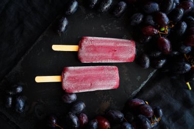 Koyu arkaplanda koyu üzüm kümelerinin yanında iki üzüm şekeri.