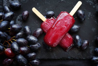 Koyu arkaplanda koyu üzüm kümelerinin yanında iki üzüm şekeri.