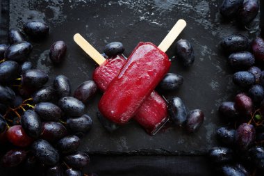 Koyu arkaplanda koyu üzüm kümelerinin yanında iki üzüm şekeri.