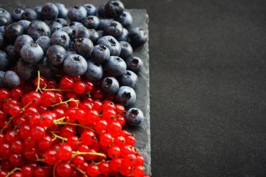 Siyah tahta üzerinde kırmızı frenk üzümü ve taze yaban mersini.