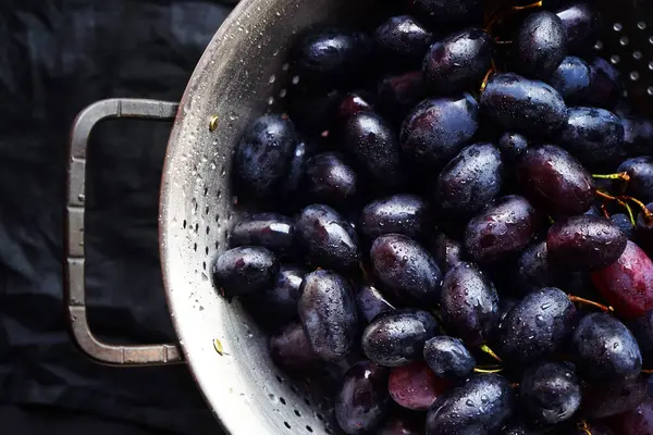 stock image Brushes of dark red grapes in an iron colander on a dark background