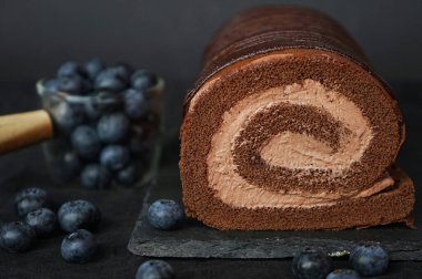 Koyu arkaplanda yabanmersininin yanında siyah tepside çikolatalı krema.