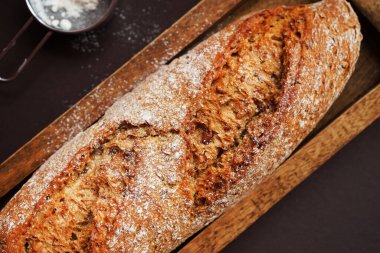 Tahta tepside taze ekmek, kahverengi zemin üzerinde un olan bir eleğin yanında.