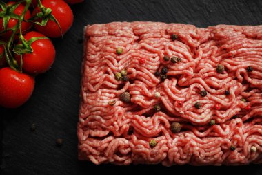 Siyah bir tepside siyah ve kırmızı biberli kıyma, koyu arkaplanda domates dalının yanında.