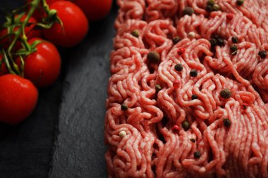 Siyah bir tepside siyah ve kırmızı biberli kıyma, koyu arkaplanda domates dalının yanında.