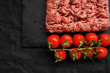 Siyah bir tepside siyah ve kırmızı biberli kıyma, koyu arkaplanda domates dalının yanında.