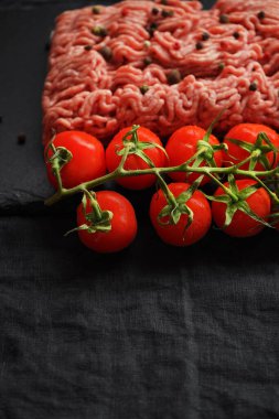 Siyah bir tepside siyah ve kırmızı biberli kıyma, koyu arkaplanda domates dalının yanında.