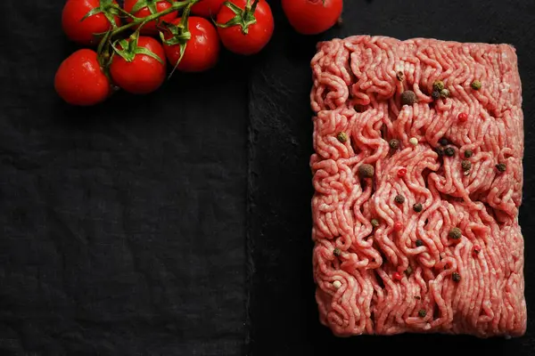 stock image Minced meat with black and red peppers on a black slate tray next to a branch of tomatoes on a dark background