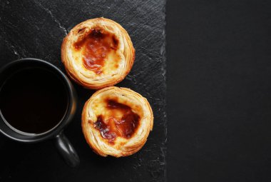 Koyu arkaplanda sade bir fincan kahvenin yanında yumurtalı tartlar.