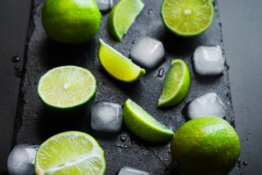 Dilimlenmiş ve tüm limonlar siyah bir zemin üzerinde buz küplerinin yanında.