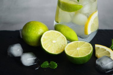 Kola, buz, nane, limon ve kireç dilimli bardak narenciye ve buz küplerini kesmek için gri bir arka planda siyah bir tepside.