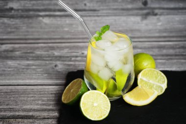 Soda, buz, limon ve kireç dilimli bardak. Gri ahşap arka planda siyah tepside narenciye meyveleri kesmek için.