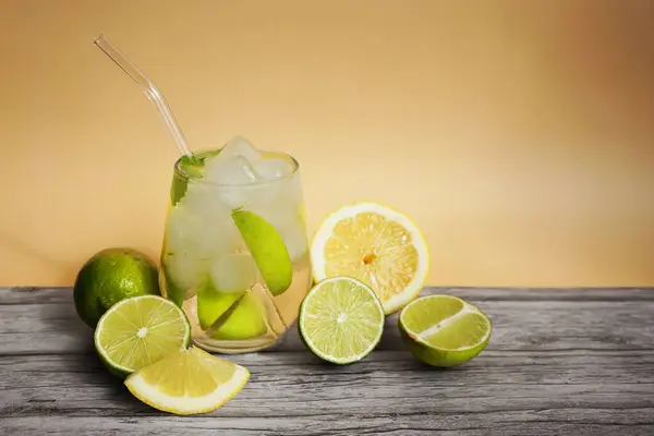 Kola, buz, limon ve kireç dilimli bardaklar parlak bej arka planda turunçgil meyveleri kesmek için.