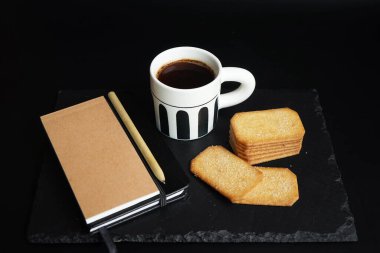 Tarçın şekerli kurabiyelerin yanında bir fincan kahve ve arka planda kalem olan not defteri.