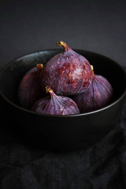 Siyah bir tabakta bütün incirleri koyu bir arka planda.