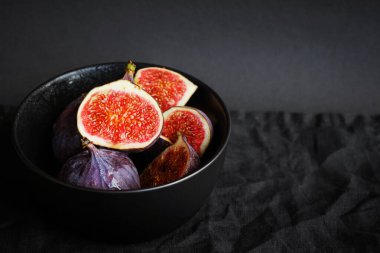 Olgunlaşmış ve dilimlenmiş incirler siyah bir tabakta karanlık bir arka planda.