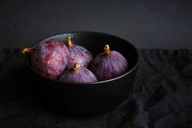 Siyah bir tabakta bütün incirleri koyu bir arka planda.