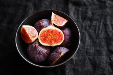 Olgunlaşmış ve dilimlenmiş incirler siyah bir tabakta karanlık bir arka planda.