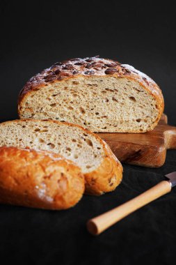 Koyu bir arka planda tahtadan parçalar kesmek için taze tahıl ekmeği.