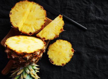 Kesilmiş taze olgun ananas parçaları. Koyu bir arka planda tahta bir tahta üzerinde.