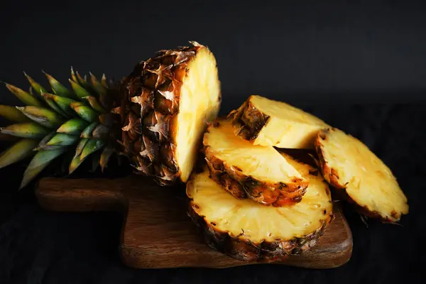 Kesilmiş taze olgun ananas parçaları. Koyu bir arka planda tahta bir tahta üzerinde.