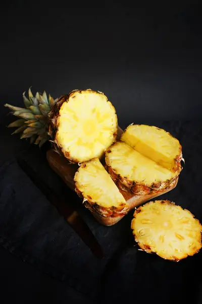 Kesilmiş taze olgun ananas parçaları. Koyu bir arka planda tahta bir tahta üzerinde.