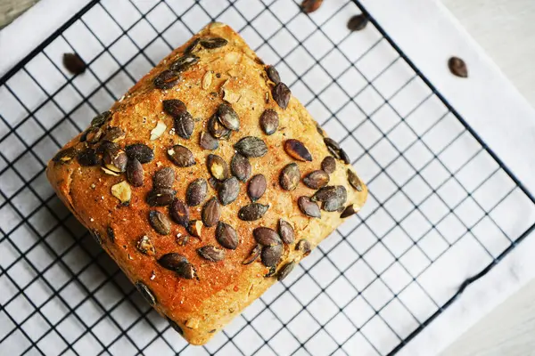 Gri arkaplandaki metal ağ tepsisinde balkabağı tohumlu bir somun taze ekmek.