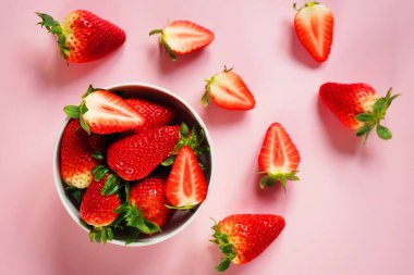 Büyük olgun çilekler beyaz bir tabakta, pembe arka planda çileklerin yanında.