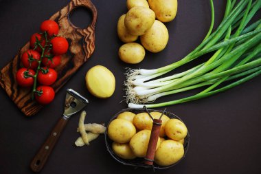 Taze domates, patates ve yeşil soğan. Arka planda sebze soyacağı yanında.