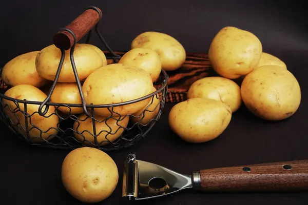 Patatesler tahtanın üzerinde sebze soyacağının yanında diğer patateslerin arka planında.