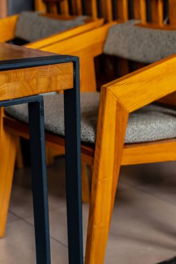 Modern bir tahta sandalye siyah metal bacaklı bir masanın altında duruyor.