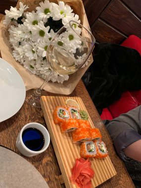 Suşi, şarap ve masanın üstünde bir buket çiçekle romantik bir akşam yemeği.