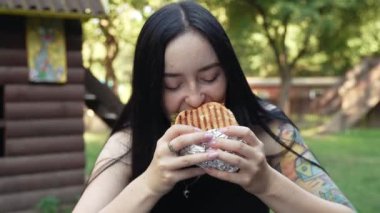 Esmer bir kız iştah açıcı bir şekilde lezzetli bir burger yer, fast food.