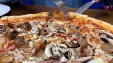 İştah açıcı büyük bir dilim pizza yavaş yavaş ve cezbedici bir şekilde tabağa uzanıyor.