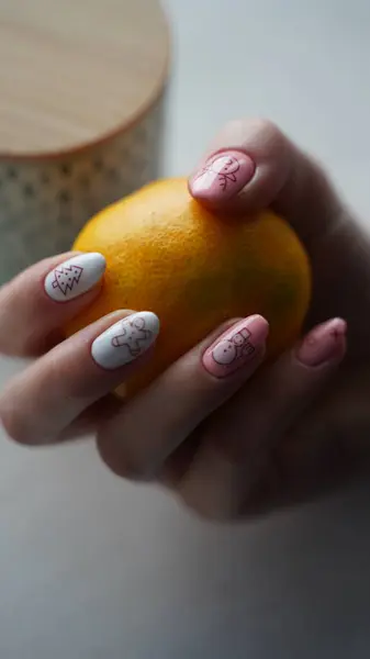 A hand with a winter manicure holds a tangerine