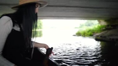 Bir göldeki köprünün altında, şapkalı genç bir kadın.