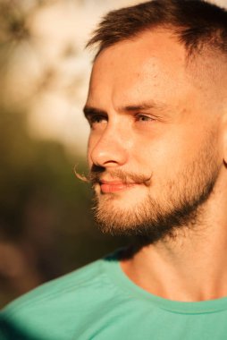 Güneş altında sakallı ve bıyıklı genç bir adam.