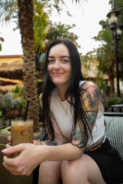 Kafede gülümseyen soğuk kahve ve dövmeli bir kadın.