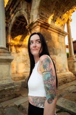 Antik bir kemerin önünde dövmeli bir kadının portresi.