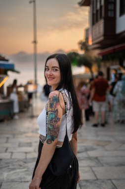 Akşamları sahilde dövmeli neşeli bir kadın turist.