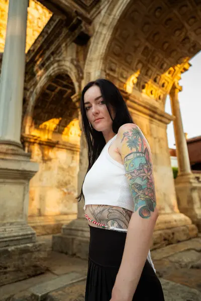 Antik bir kemerin önünde dövmeli bir kadının portresi.