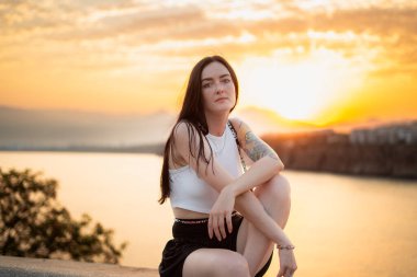 Esmer kız gün batımında kayalarda oturuyor.