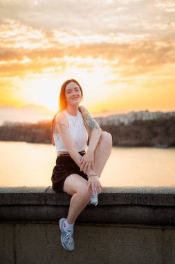 Neşeli kadın gün batımında köprüde oturuyor.