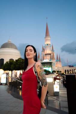 Akşam karanlığında kırmızı elbiseli kadın masal kalesinin önünde poz veriyor.