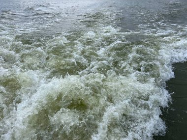 Beyaz çalkantılı okyanus dalgalarının yakın bir fotoğrafı çarpar ve köpüklü beyaz suyun güçlü bir görüntüsünü oluşturur. Okyanus üstü bulutlu bir günde okyanusta bir feribottan alınan derin ve karanlık denize karşı.