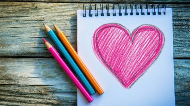 Yanındaki renkli kalemlerle kağıda çizilmiş renkli bir kalp.