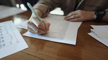 Kişi, detaylara ve organizasyona dikkat eden belgeler üzerine odaklanır. ayarlar ofis veya çalışma ortamı gibi görünüyor, kağıtlar ve ahşap masa görünür.